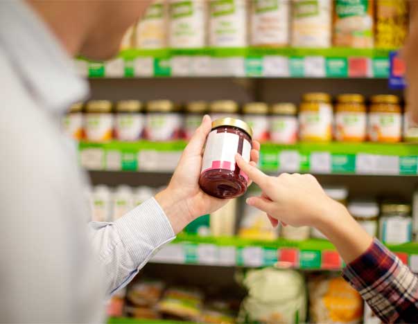 People looking at the label on a jar in a grocery store.