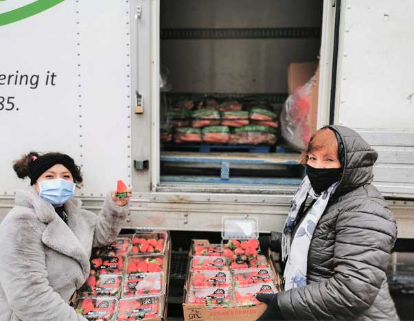 Two people holding crates of strawberries in front of a truck.