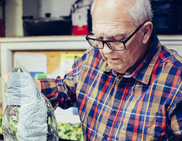 Elderly man holding a bag of vegetables.